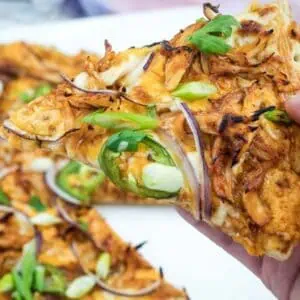 A hand holding a slice of BBQ chicken pizza.