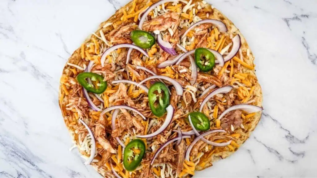 Unbaked BBQ chicken pizza topped with chopped red onion, jalapeno, and cheese.