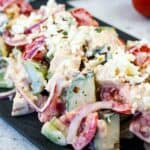 A plate of chopped salad with cucumbers, tomatoes, red onions, feta cheese, and creamy dressing on a dark rectangular serving dish.