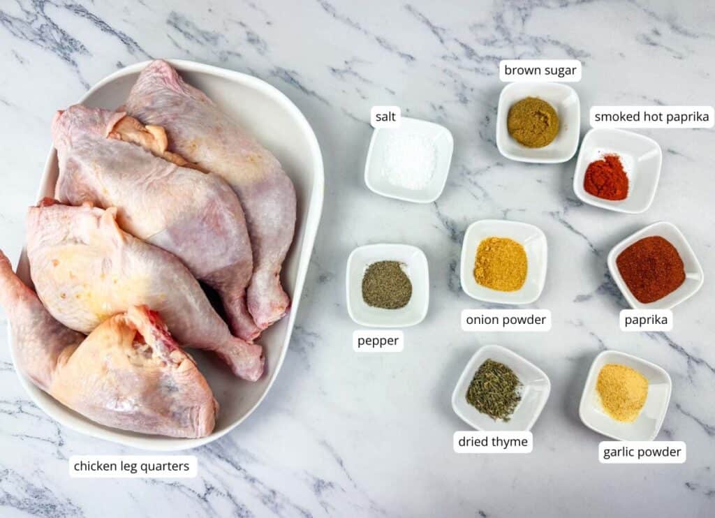 Raw chicken leg quarters on a plate next to small bowls containing salt, pepper, dried thyme, onion powder, garlic powder, brown sugar, smoked hot paprika, and paprika.