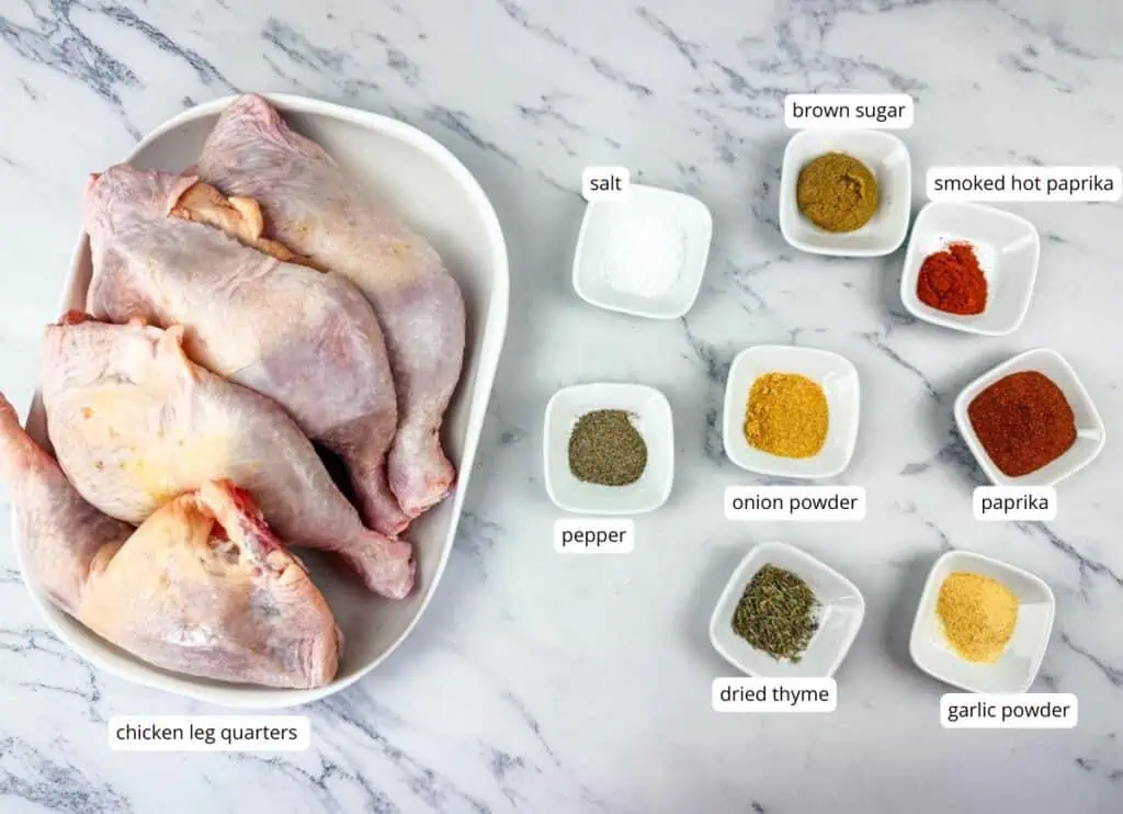Raw chicken leg quarters on a plate next to small bowls containing salt, pepper, dried thyme, onion powder, garlic powder, brown sugar, smoked hot paprika, and paprika.