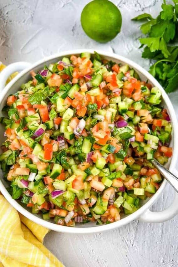 Shirazi Salad in a white bowl with parsley and lime in the background.