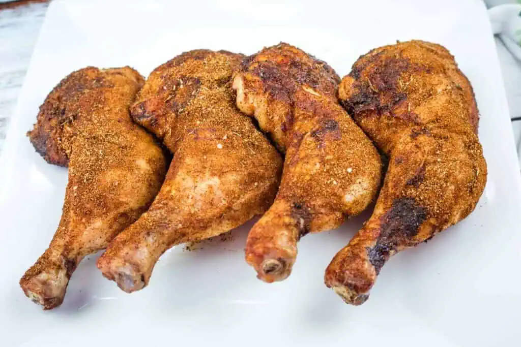 Four seasoned and cooked chicken leg quarters arranged in a row on a white plate.