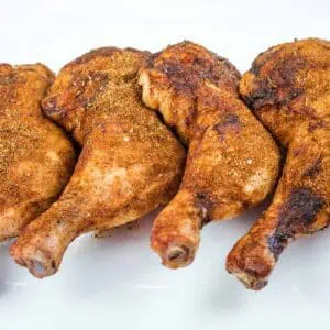 Four seasoned and cooked chicken leg quarters arranged in a row on a white plate.