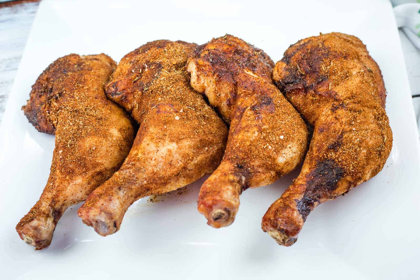 Four Smoked Chicken Leg Quarters are arranged in a row on a white plate.