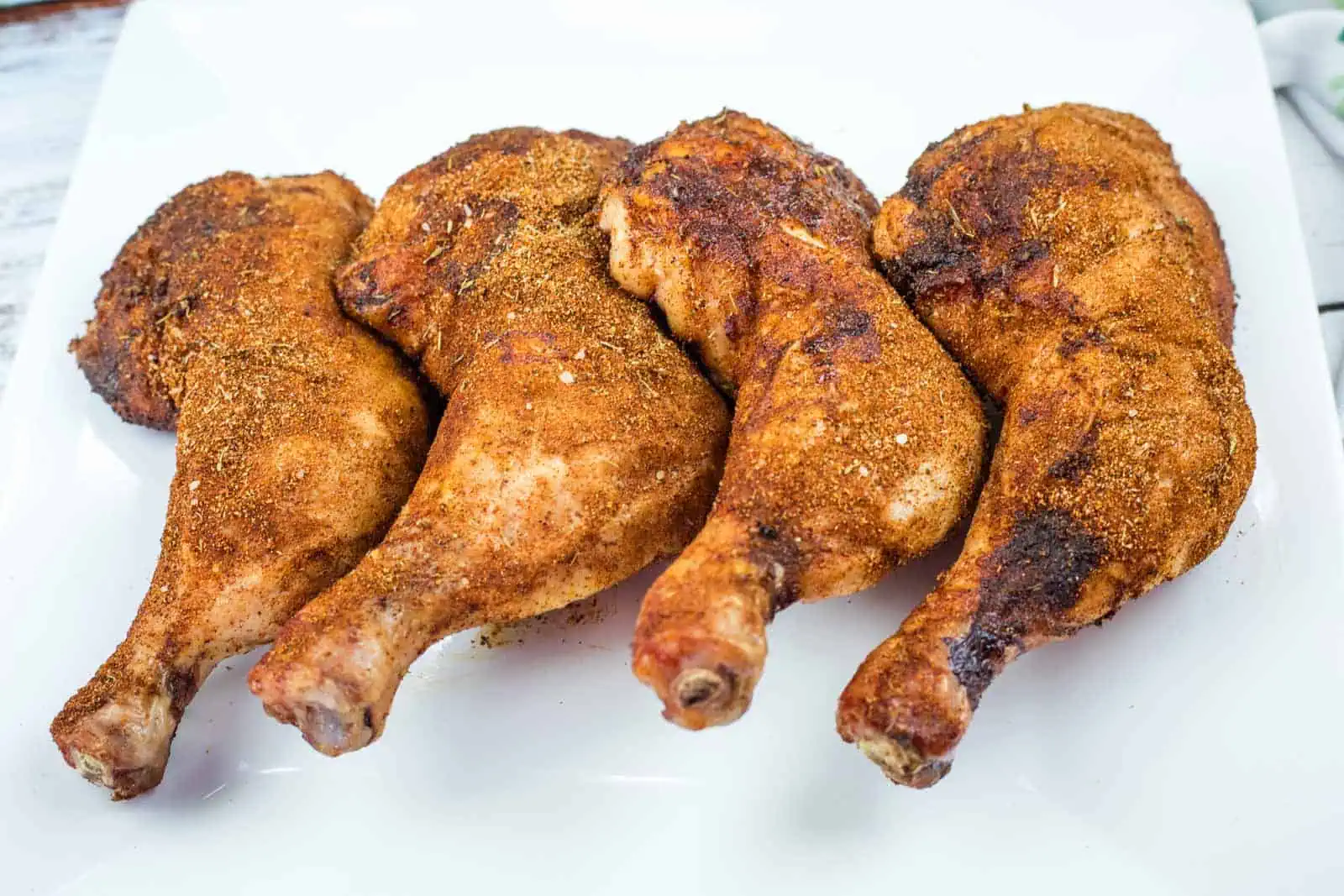 Four Smoked Chicken Leg Quarters are arranged in a row on a white plate.