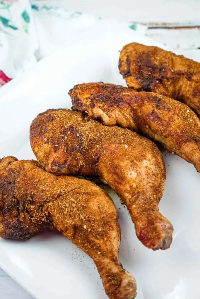 Four seasoned, baked chicken legs arranged on a white rectangular plate.