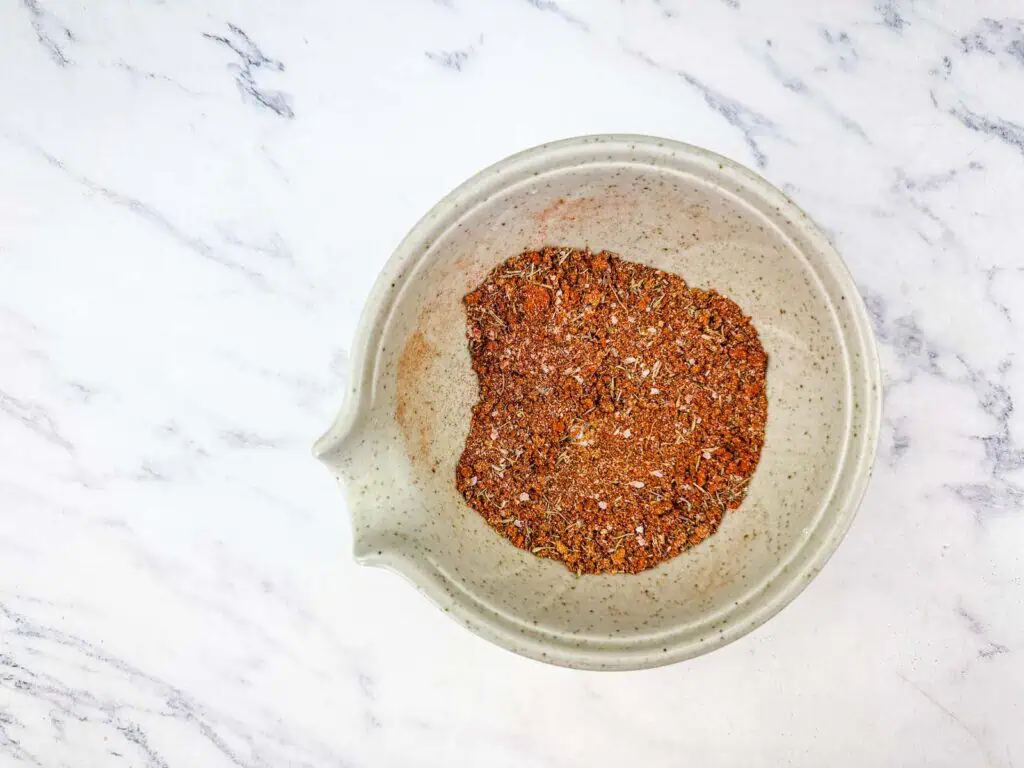 A white bowl containing a blend of various ground spices sits on a white marble surface.