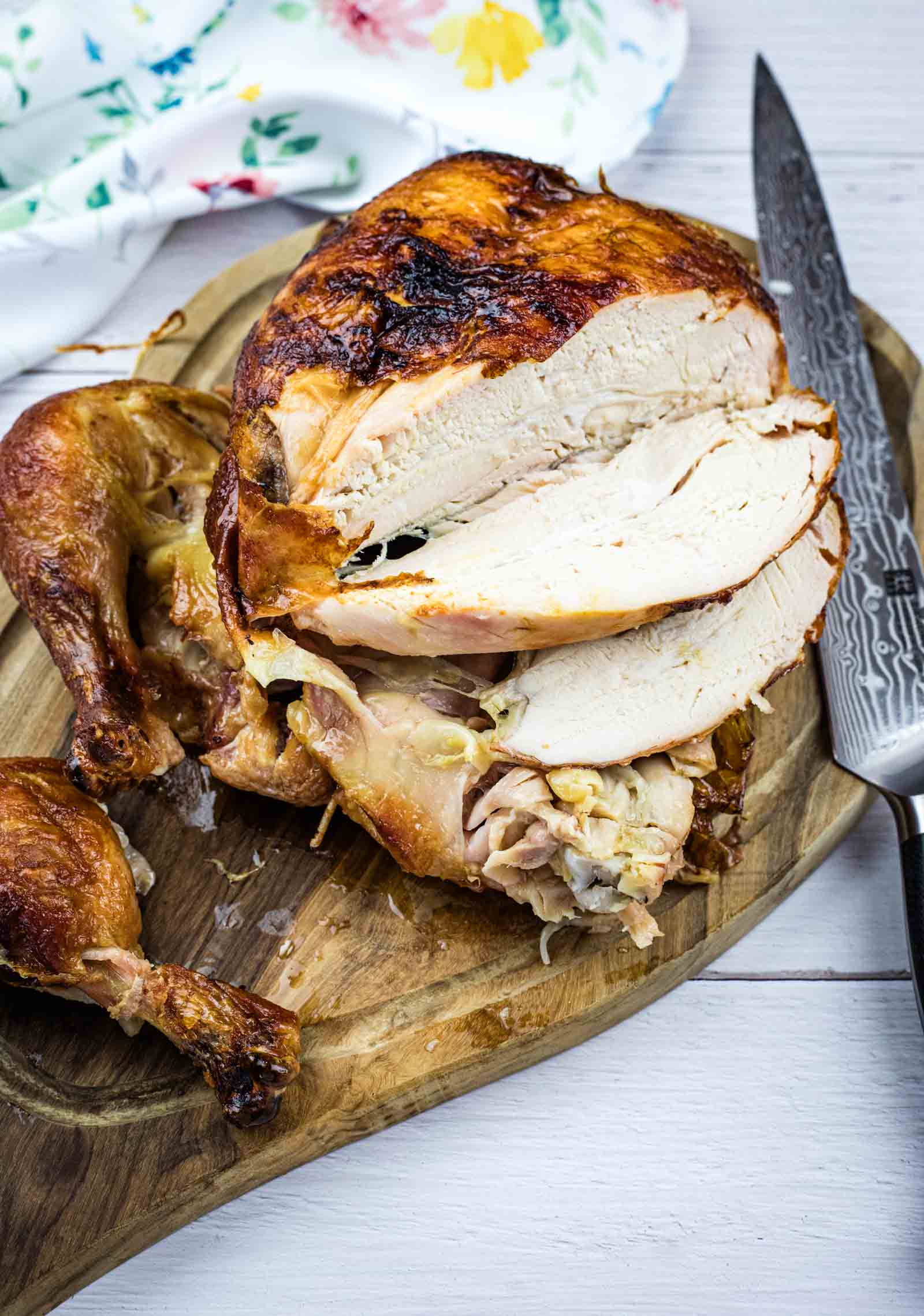 A cooked, partially carved roast chicken sits on a wooden cutting board with a knife beside it.