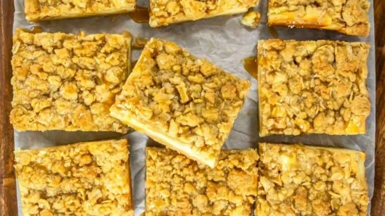 Nine oatmeal crumb bars arranged on parchment paper, with a golden brown crumb topping and visible caramel drizzle.
