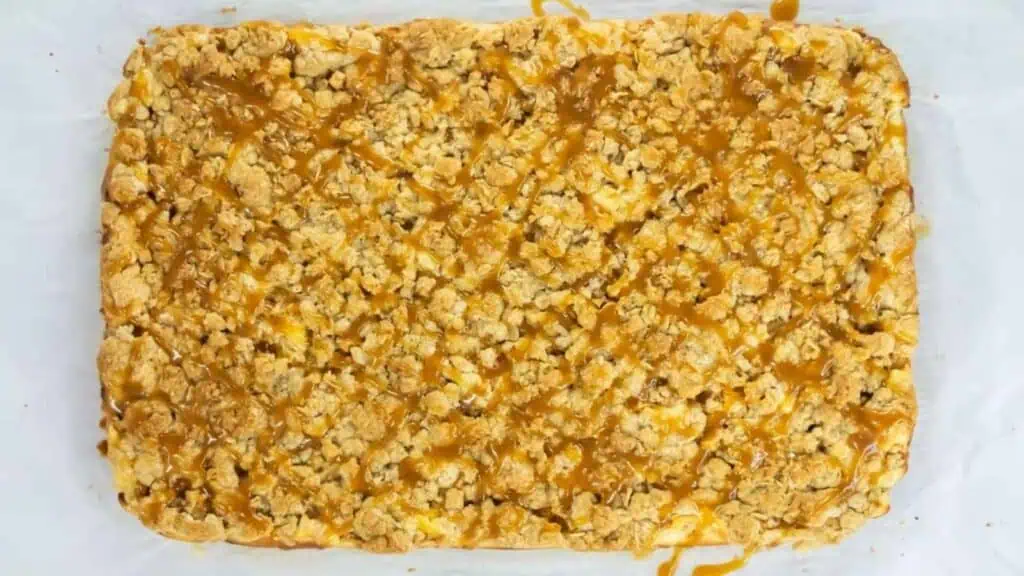 A rectangular oat crumble dessert on parchment paper, drizzled with caramel sauce.