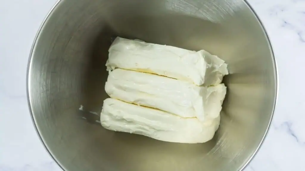 Three blocks of cream cheese in a stainless steel mixing bowl, viewed from above.