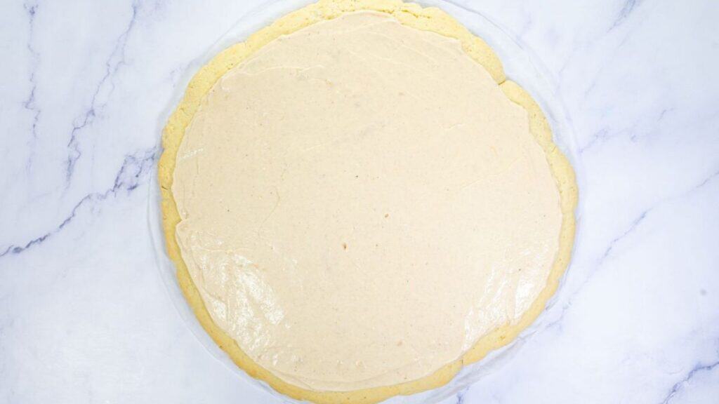 A round, baked crust topped with a smooth, light beige cream layer on a white marble surface.