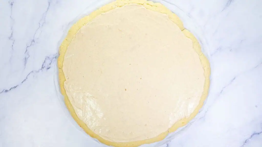 A round, baked crust topped with a smooth, light beige cream layer on a white marble surface.