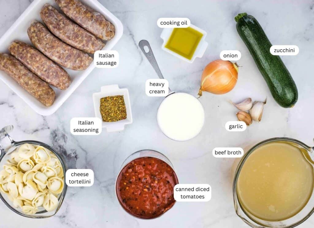 Top-down view of recipe ingredients: Italian sausage, cheese tortellini, Italian seasoning, canned diced tomatoes, beef broth, heavy cream, cooking oil, onion, garlic, and zucchini.