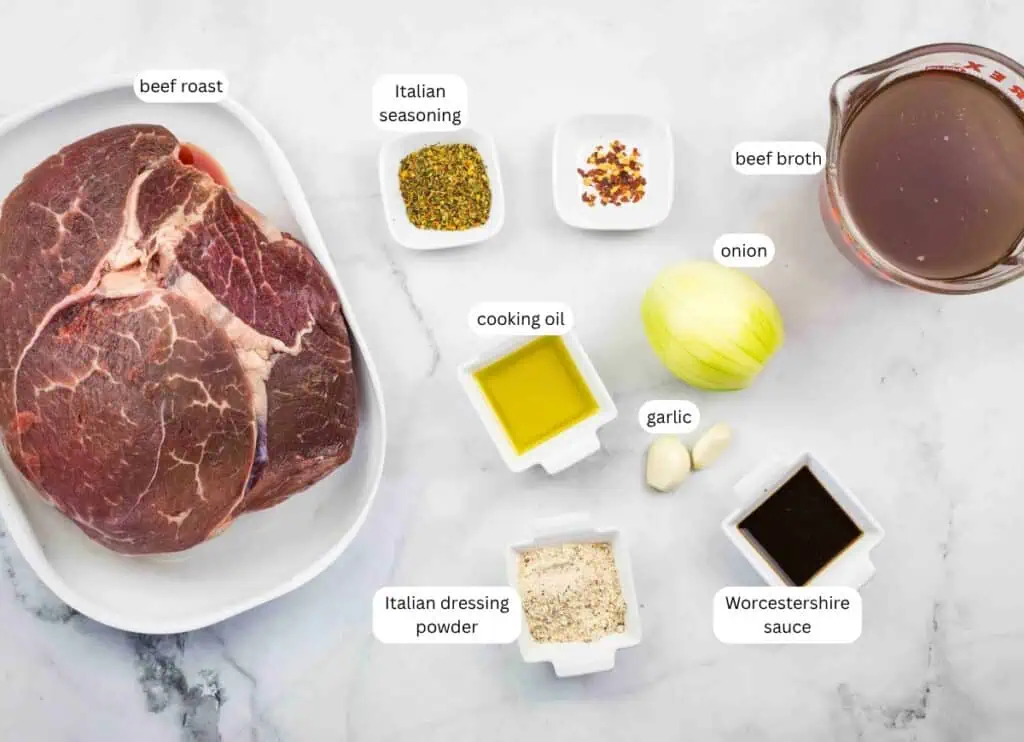 Top-down view of beef roast, Italian seasoning, beef broth, cooking oil, onion, garlic, Italian dressing powder, and Worcestershire sauce arranged on a marble surface, each labeled.