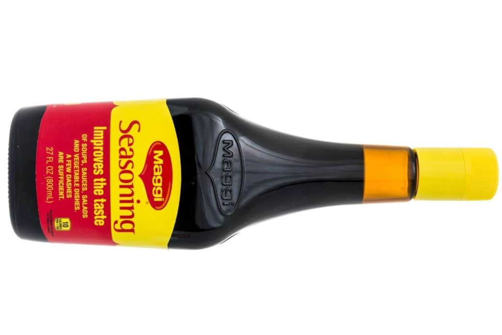 A bottle of Maggi Seasoning Sauce with a yellow and red label, lying on its side with a yellow cap.