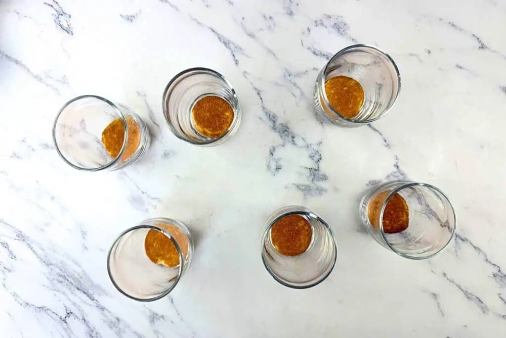 Six empty glasses with a small amount of brown liquid at the bottom, arranged on a white marble surface.