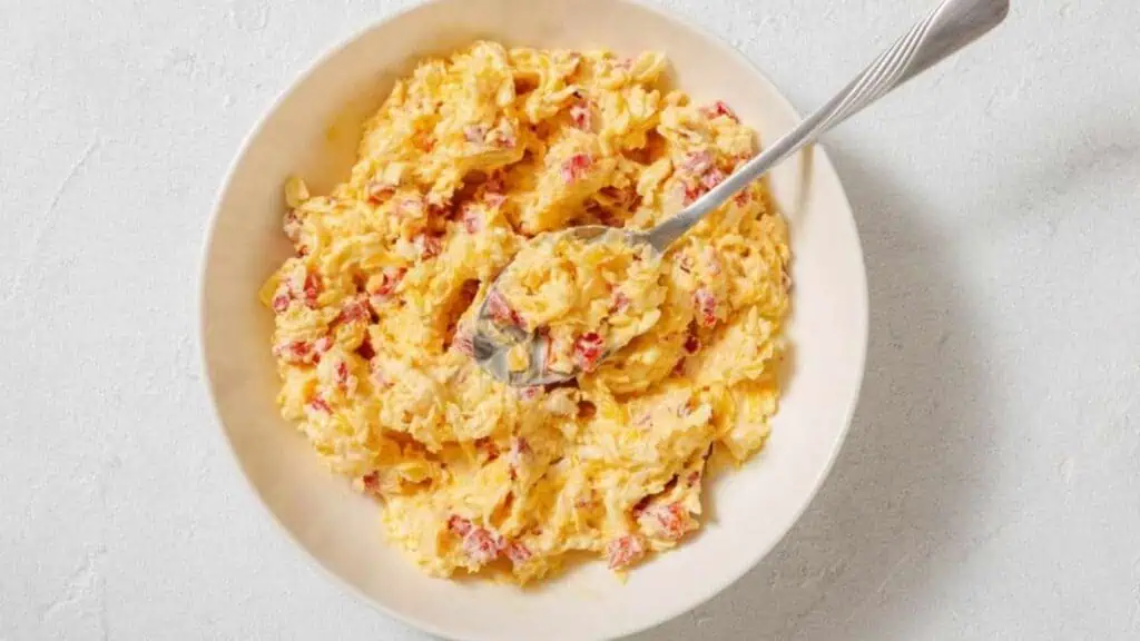 A bowl of scrambled eggs mixed with diced red bell peppers, with a fork resting in the mixture.