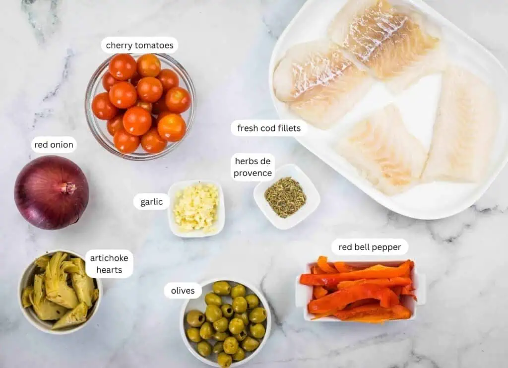 Ingredients including fresh cod fillets, cherry tomatoes, red onion, garlic, artichoke hearts, olives, red bell pepper, and herbs de Provence arranged on a marble surface.