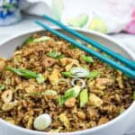 A bowl of fried rice with scrambled egg, sliced scallions, and crispy garlic, served with teal chopsticks on the side.