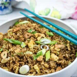 A bowl of fried rice with scrambled egg, sliced scallions, and crispy garlic, served with teal chopsticks on the side.