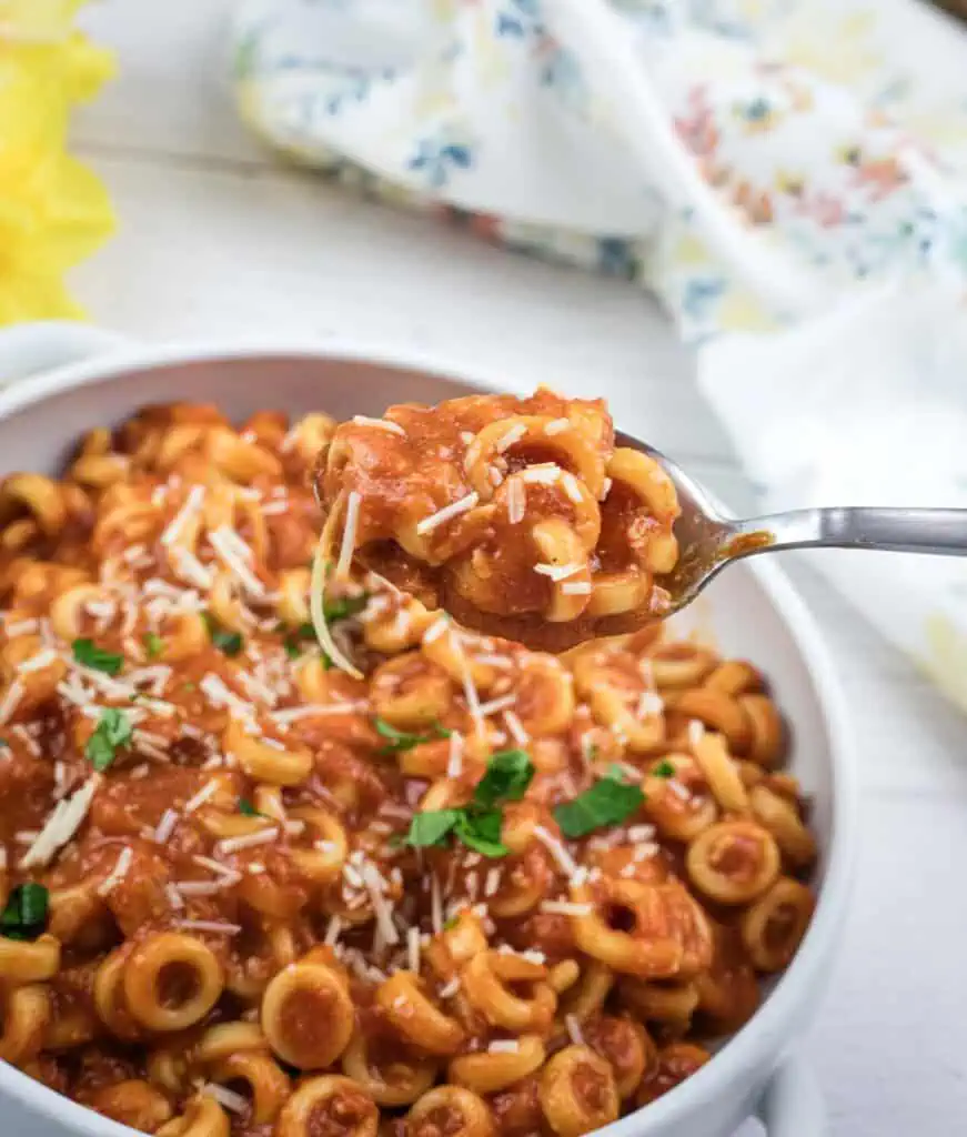 A bowl of pasta with tomato sauce and grated cheese, garnished with parsley. A fork holds a bite-sized portion above the bowl.