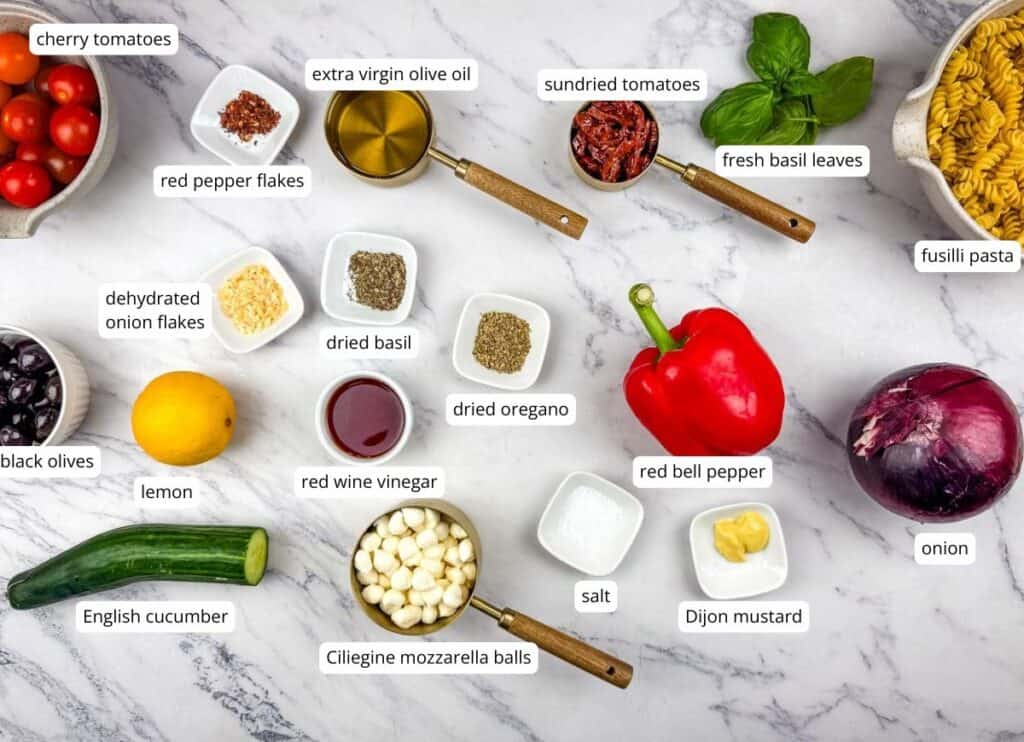 A flat lay of various labeled ingredients on a marble surface, including vegetables, spices, pasta, cheese, olive oil, and vinegar.