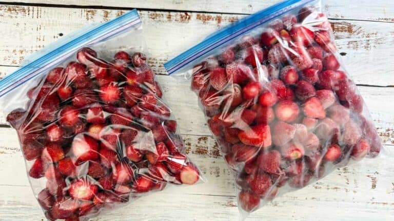 Two clear zip-top bags filled with frozen strawberries are placed on a white wooden surface.