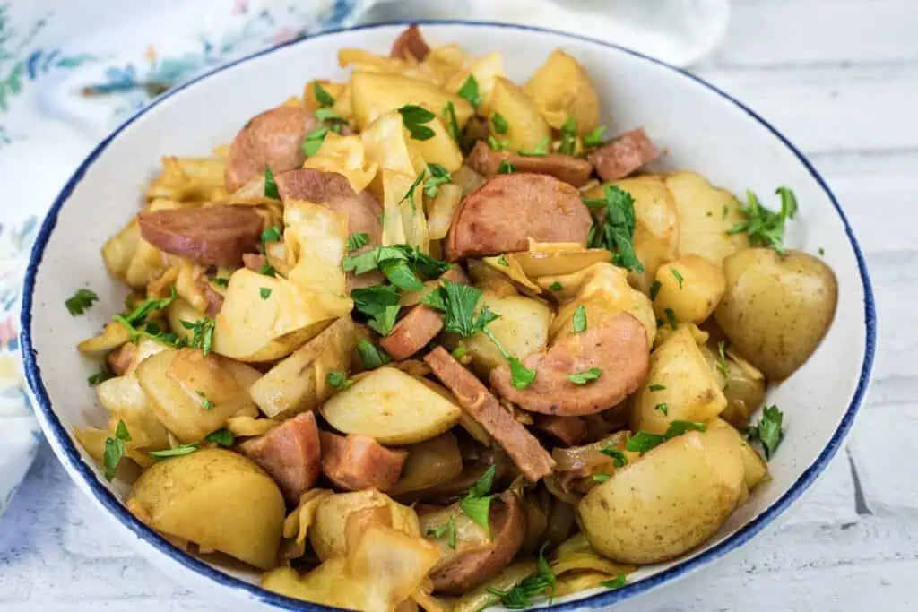 A bowl filled with sliced sausage, potatoes, and cabbage, garnished with chopped parsley.