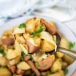 A spoonful of cooked potatoes, sausage, and cabbage held above a bowl filled with the same mixture, garnished with parsley.