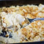 A spoonful of creamy baked chicken casserole held above a pan filled with the same dish.