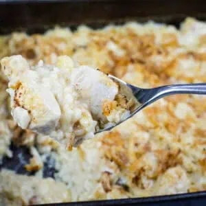 A spoonful of creamy baked chicken casserole held above a pan filled with the same dish.