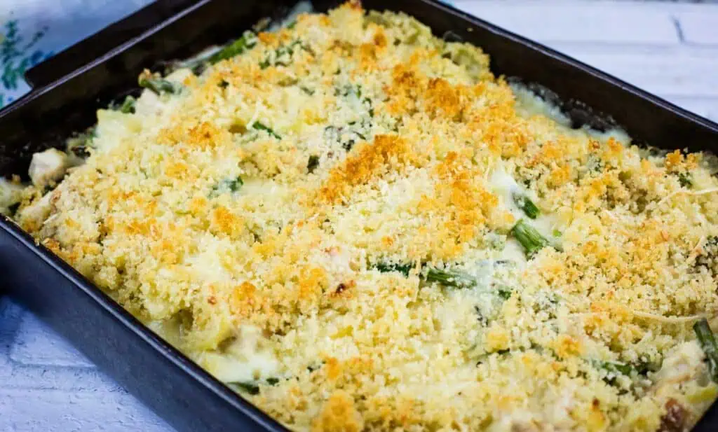 A rectangular baking dish filled with a baked casserole topped with golden brown breadcrumbs and visible pieces of green vegetable.