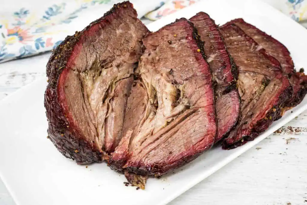 Three thick slices of smoked beef brisket are arranged on a white plate, showing a dark crust and juicy, tender interior.