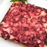 A square-shaped baked dessert with a golden crust, topped with a layer of baked strawberries, on a white plate.