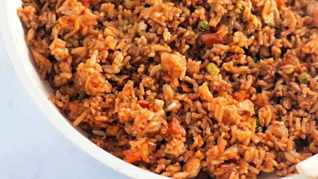 A close-up of cooked fried rice with vegetables, including peas and carrots, served in a white dish.