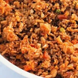 A close-up of cooked fried rice with vegetables, including peas and carrots, served in a white dish.