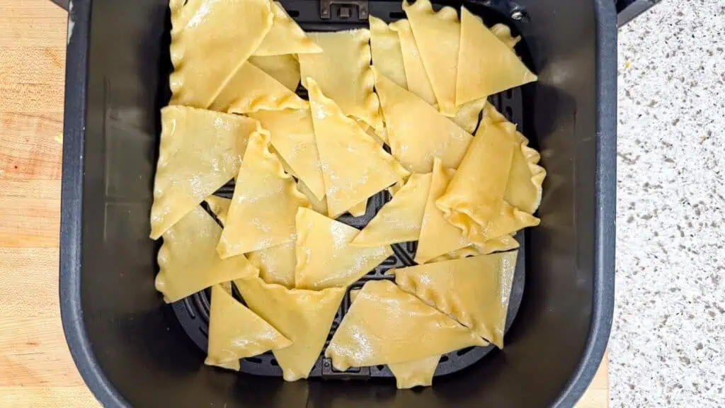 Uncooked lasagna noodle pieces arranged in a single layer inside an air fryer basket.
