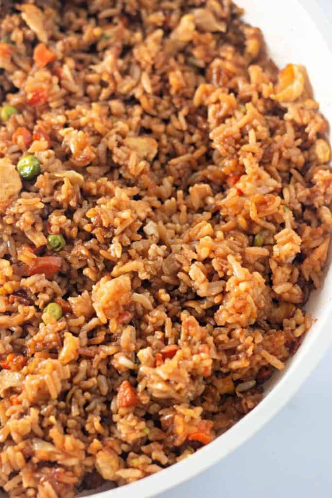 Close-up of a large serving of fried rice with vegetables, including peas and carrots, mixed with scrambled eggs in a white pan.
