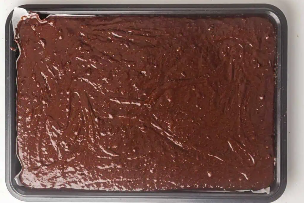 A rectangular baking tray filled with an even layer of chocolate brownie batter, ready to be baked.