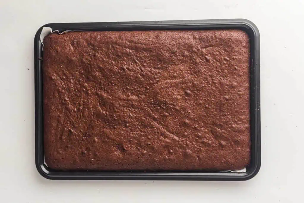 A rectangular tray of uncut baked chocolate brownies sits on a white surface.