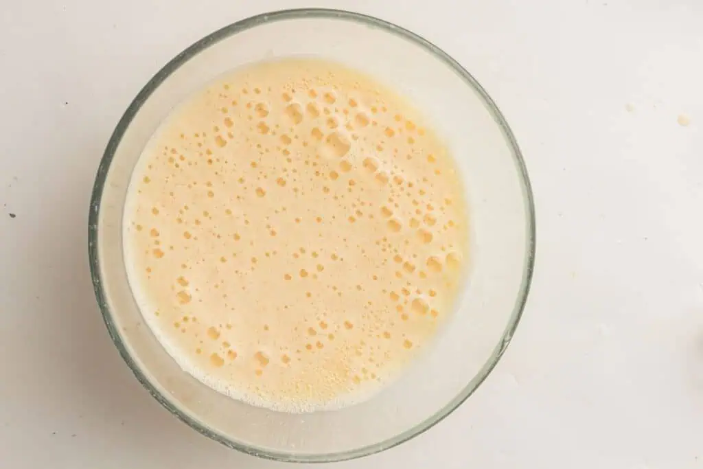 A glass bowl filled with frothy, beaten eggs on a white surface.