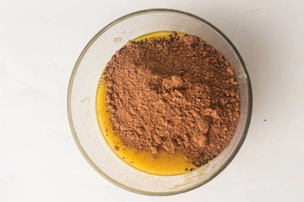 A glass bowl containing yellow batter with a mound of cocoa powder on top, viewed from above on a white surface.