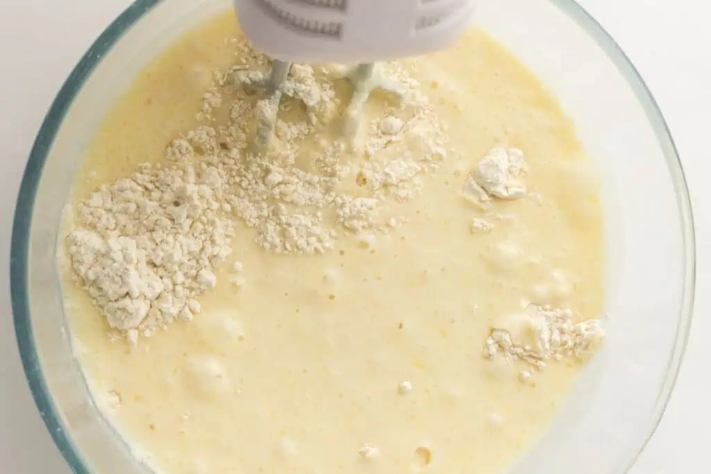 An electric hand mixer blending flour and wet ingredients in a glass mixing bowl.