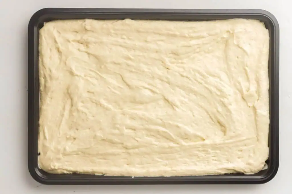 A rectangular baking tray filled with an even layer of uncooked cake batter on a white surface.