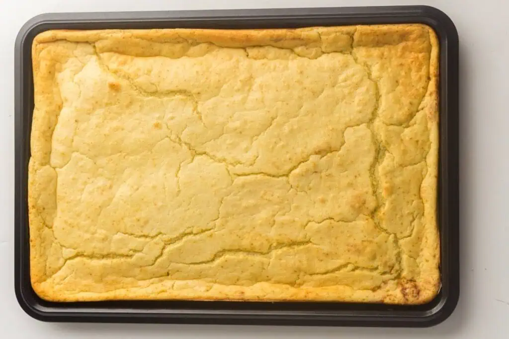 A rectangular cornbread in a baking pan with a golden, slightly cracked surface, viewed from above.