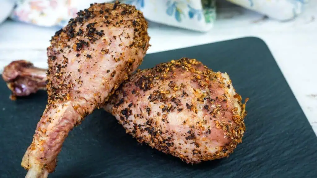 Two seasoned and cooked turkey legs are placed on a dark slate board.