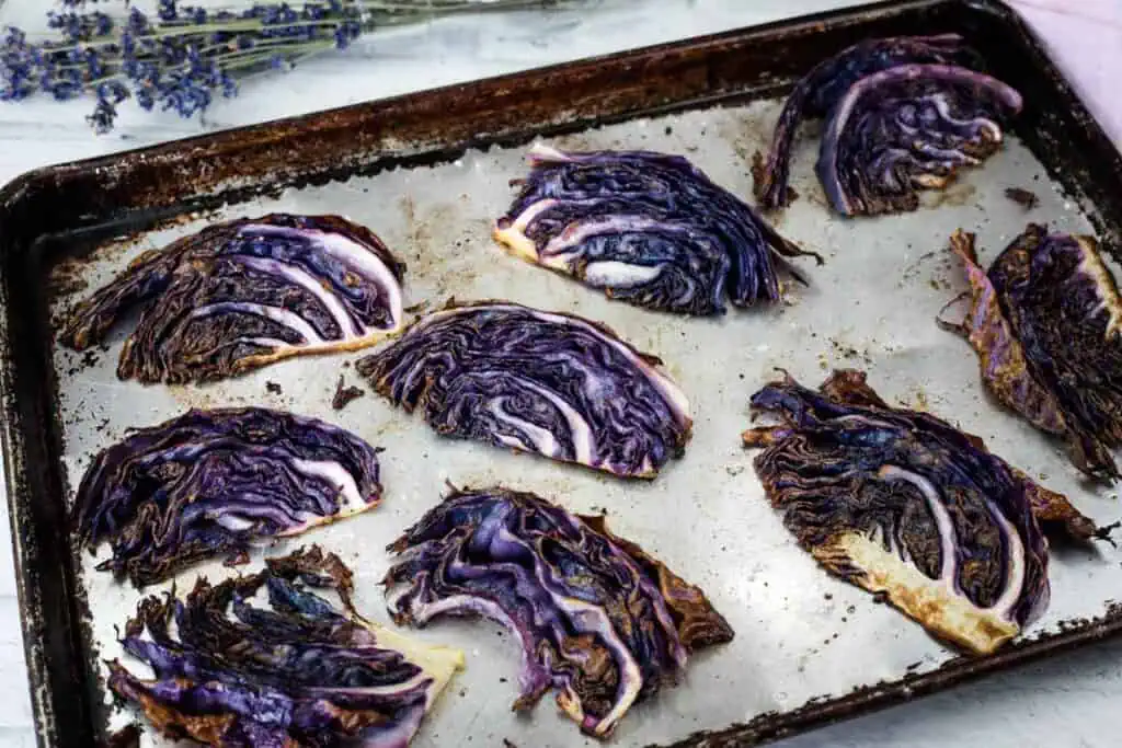Slices of roasted purple cabbage on a metal baking sheet, with some grilled edges. A sprig of dried lavender lies in the background.