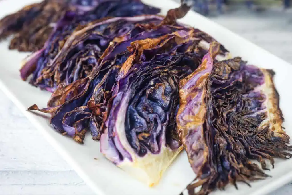Sliced roasted purple cabbage arranged on a white rectangular plate, showing charred and crispy edges.